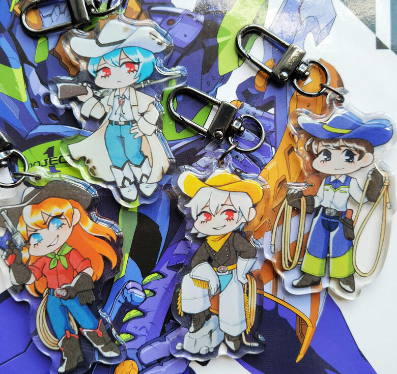 NGE Cowboys photograph of four acrylic charms on a neon genesis light novel. the charms are the NGE child pilots dressed up as cowboys