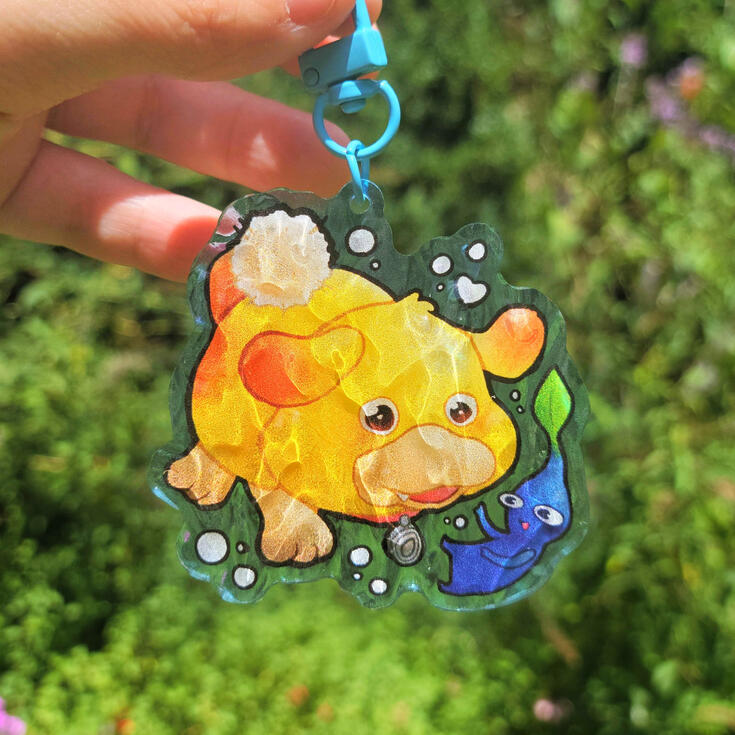 photograph of two acrylic keychains sitting on a cook book. the keychains are fidough and dachsbun