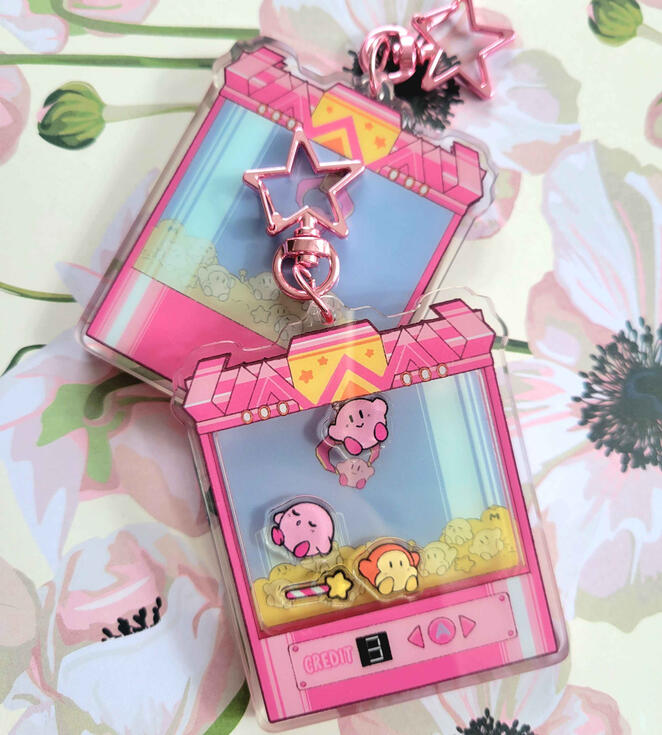 Kirby Shaker a photograph of a shaker charm. the shaker charm depicts a kirby UFO crane game inspired by kirbys adventure crane fever