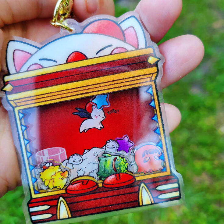 Moogle Shaker photograph of an acrylic shaker charm inspired by the moogles paw UFO mini game in ffxiv gold saucer. inside are shakers depicting a chocobo goobbue and bomb doll