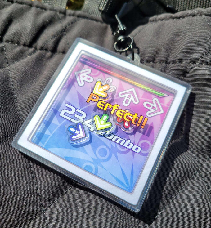 DDR Shaker photograph of a shaker charm that is inspired by dance dance revolutions play screen. the photo shows the front of the shaker charm. the shakers inside look like ddr arrows